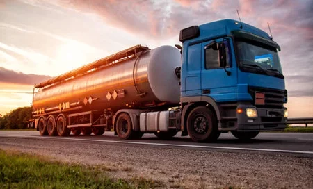 183054926-a-blue-modern-truck-with-a-semi-trailer-tanker-transports-dangerous-goods-against-the-backdrop-of-th